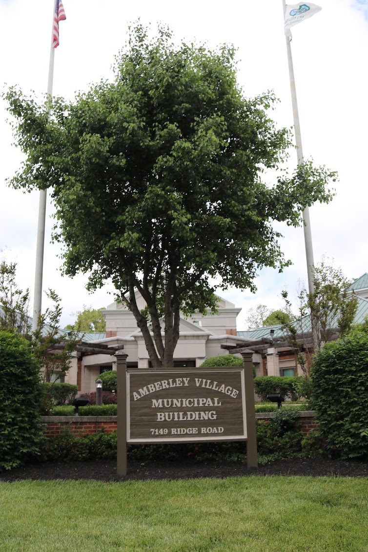 Signage at front of Amberley Village Municipal Building surrounded by trees and greenery