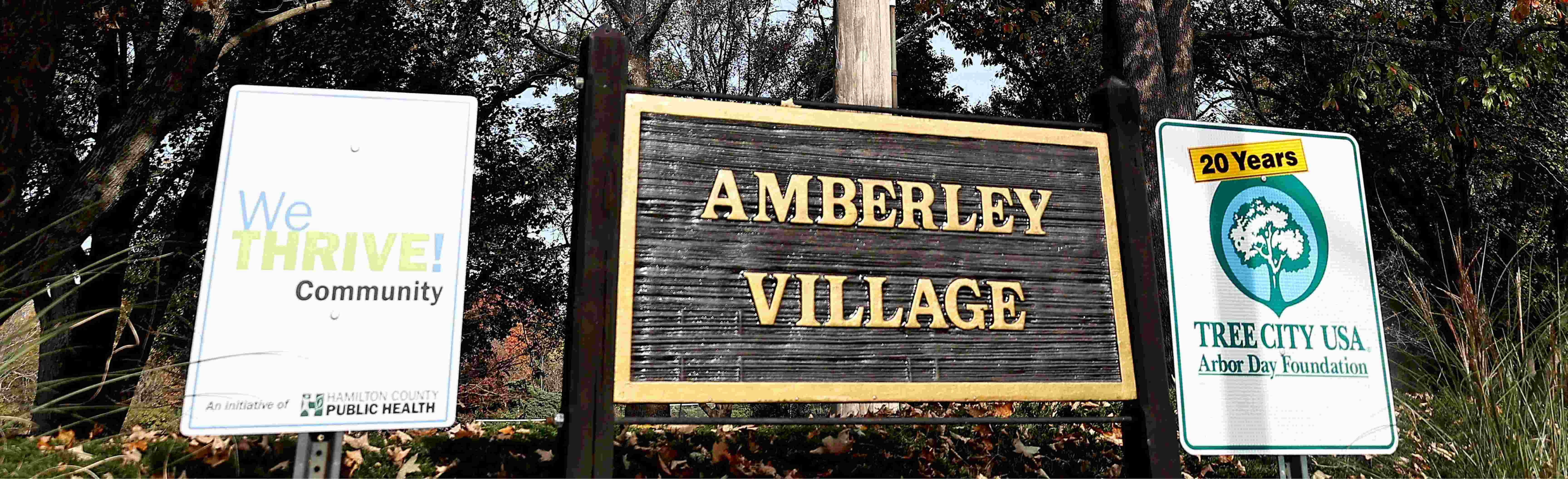 Amberley Village signage nestled between signs indicating we are a WeTHRIVE community and a Tree City USA